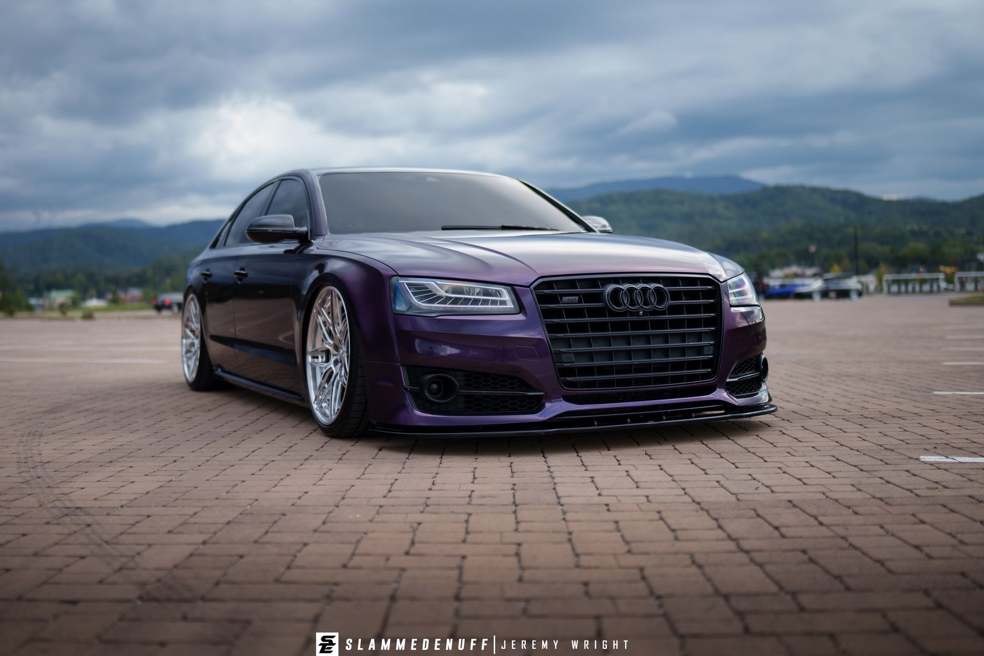Purple luxury sedan with custom wheels parked on brick pavement with mountains in the background.